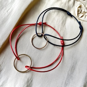 May include: Two intertwined cords with gold rings. One cord is red and the other is black.