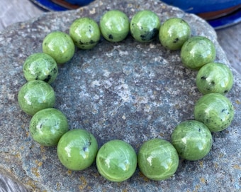 May include: A green jade stone bracelet with round beads. The bracelet is on a gray stone surface.