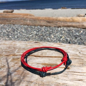 May include: A red and dark blue leather bracelet with a knotted design. The bracelet is on a wooden surface.
