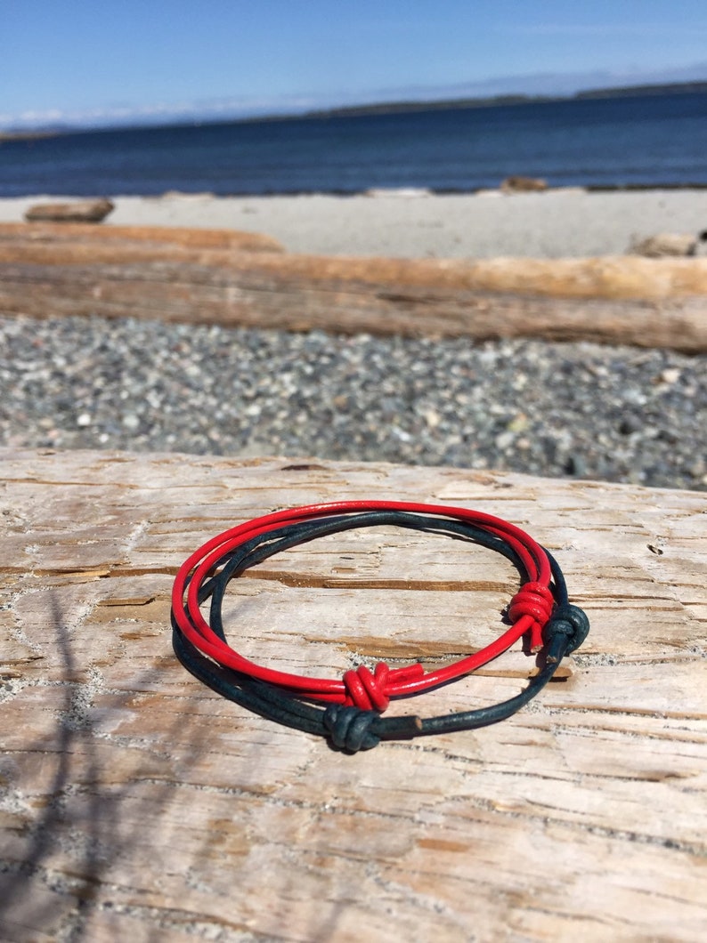 May include: A red and dark blue leather bracelet with a knotted design. The bracelet is on a wooden surface.