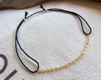 May include: A black cord bracelet with a gold chain accent. The bracelet features a delicate gold chain section and adjustable black cords with gold beads. The jewelry is displayed on a neutral fabric background.