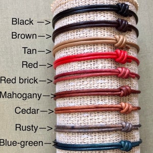 May include: A display of ten leather bracelets in various colors, including black, brown, tan, red, red brick, mahogany, cedar, rusty, and blue-green. Each bracelet is tied with a knot at the end.