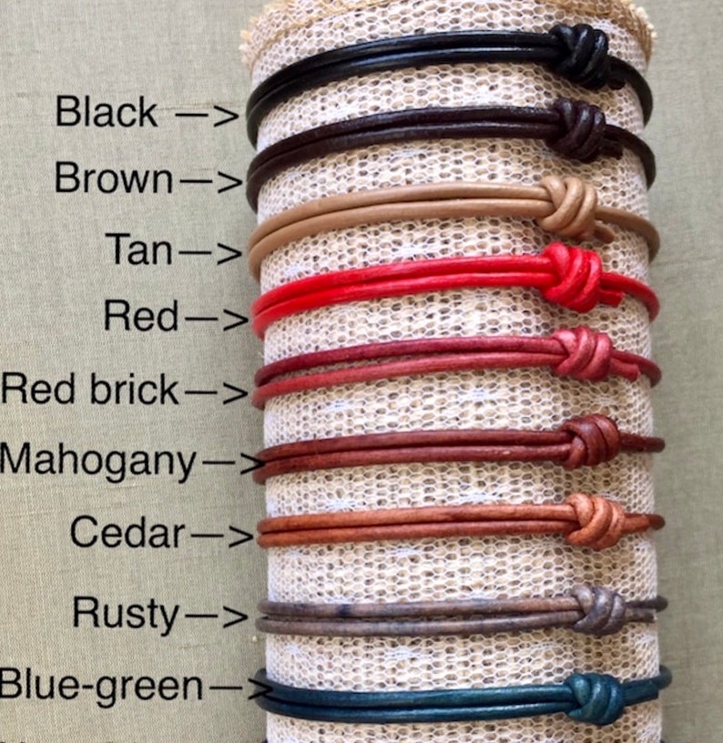 May include: A display of ten leather bracelets in various colors, including black, brown, tan, red, red brick, mahogany, cedar, rusty, and blue-green. Each bracelet is tied with a knot at the end.