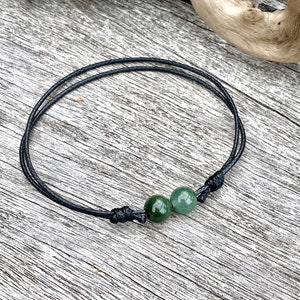 May include: A black cord bracelet with two green jade beads.