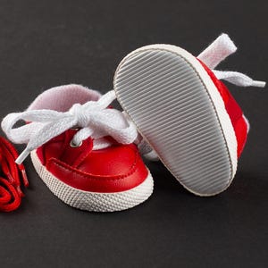 Op de afbeelding: Een paar kleine rode babysneakers met witte veters en zolen. De schoenen hebben een klassiek ontwerp, met een rood bovenwerk, witte rand en een getextureerde witte zool. De veters zijn gestrikt.