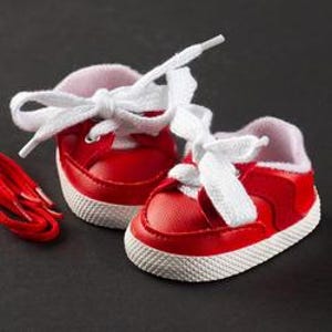 Op de afbeelding: Kleine rode sneakers met witte veters en zolen, geschikt voor een baby of pop. De schoenen hebben een zachte, roze voering en worden geleverd met een extra set rode veters. De sneakers zijn ongeveer 7,6 cm lang.