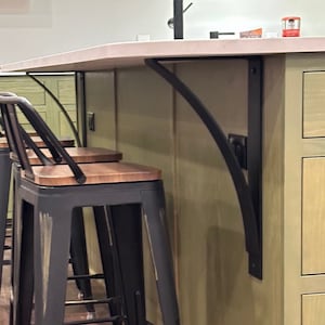 May include: Black metal brackets supporting a countertop with a white surface. Three black metal bar stools with wooden seats are in the foreground.