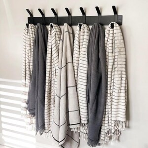 May include: A black metal rack with seven hooks holds a variety of striped and patterned towels. The towels are in shades of white, gray, and black.