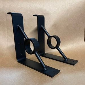 May include: Two black metal shelf brackets with a decorative angled support bar and a round ring. The brackets are designed for mounting shelves or other objects.