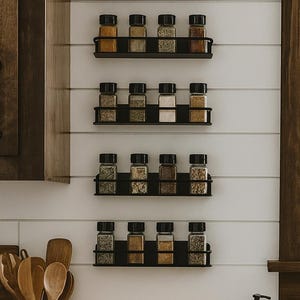 May include: A kitchen scene featuring a wooden countertop with a gas stove, a ceramic utensil holder, and a dark brown soap dispenser. Black metal spice racks hold glass jars filled with various spices. A window and dark wood cabinets are in the background.