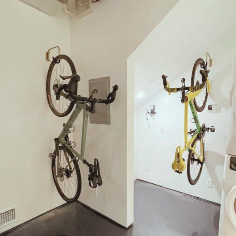 May include: Two bicycles are mounted on a wall using a hook system. The bicycle on the left is black and green, while the bicycle on the right is yellow and green.