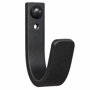 May include: A matte black metal wall hook with a J-shaped profile. The vertical mounting plate features a circular screw hole at the top and a small, rounded black decorative cap covering the upper attachment point, providing a clean finish.