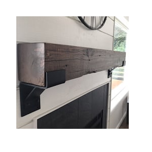 May include: A dark brown wooden mantel shelf with black metal brackets. The shelf is mounted above a black fireplace.