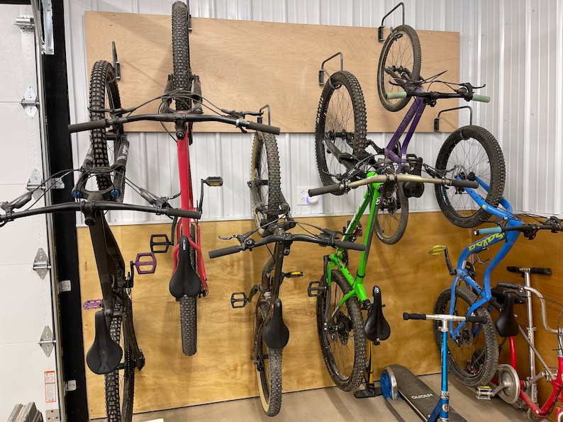 May include: Five bicycles are mounted on a wall using a wall-mounted bike rack system. The bikes are a mix of colors, including black, red, green, purple, and blue. The bikes are all mountain bikes with knobby tires.