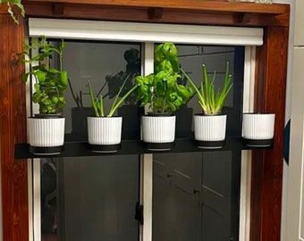May include: A black metal shelf with five white ceramic pots holding various plants, including herbs, mounted on a windowsill with a wooden frame.