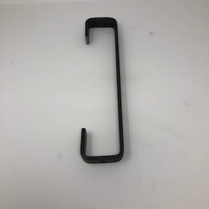 May include: A black metal hook with a rectangular shape. The hook has a long, straight vertical section connecting two shorter, horizontal sections that form a U-shape. The object is set against a white background.