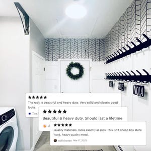 May include: Black metal coat rack with hooks mounted on a white wall. The wall has a black and white chevron pattern wallpaper. The rack has three labels: "Race", "Miles", and "Nola".