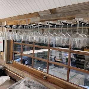 May include: A wooden wall with a metal wine glass rack holding many clear glass wine glasses. The rack is mounted above a window with multiple panes. The number 125 is visible on the window.