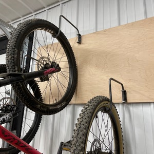 May include: Two bicycles are hanging on a wall using metal hooks. The bikes are both black with pink accents. The wall is made of wood and has a light brown color.