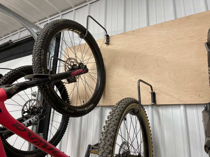 May include: Two bicycles are hanging on a wall using metal hooks. The bikes are both black with pink accents. The wall is made of wood and has a light brown color.
