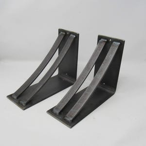 May include: Two black metal shelf brackets with a curved design. The brackets are made of heavy-duty steel and are designed to support a variety of shelves.