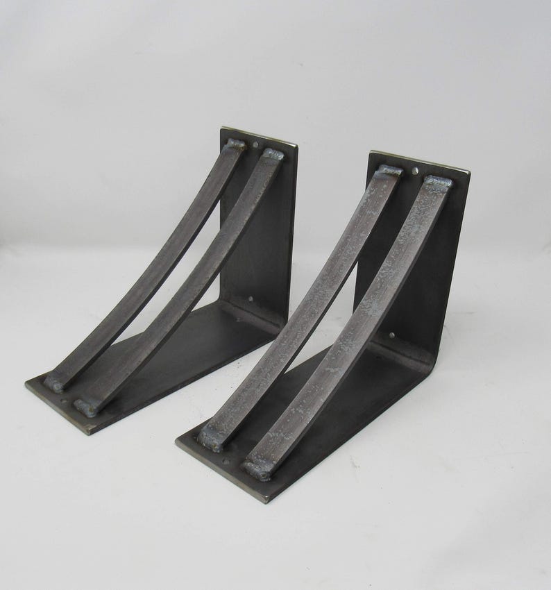 May include: Two black metal shelf brackets with a curved design. The brackets are made of heavy-duty steel and are designed to support a variety of shelves.