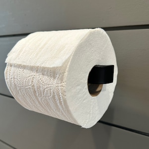 May include: A white paper towel roll on a black metal holder mounted on a gray wall.