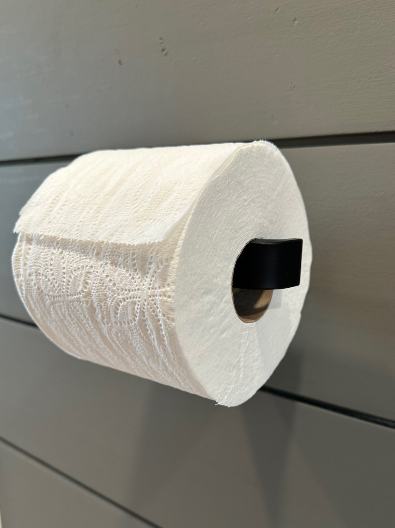 May include: A white paper towel roll on a black metal holder mounted on a gray wall.