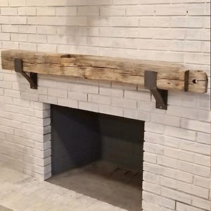 May include: A rustic wooden mantel shelf with metal brackets, mounted above a white brick fireplace.