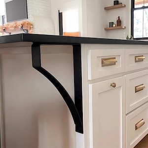 May include: Black metal bracket supporting a white kitchen island with drawers and gold hardware.