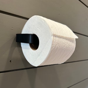 May include: A black metal paper towel holder mounted on a wall with a white paper towel roll attached.