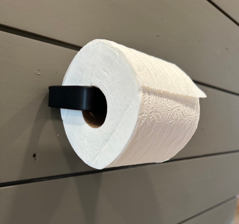 May include: A black metal paper towel holder mounted on a wall with a white paper towel roll attached.