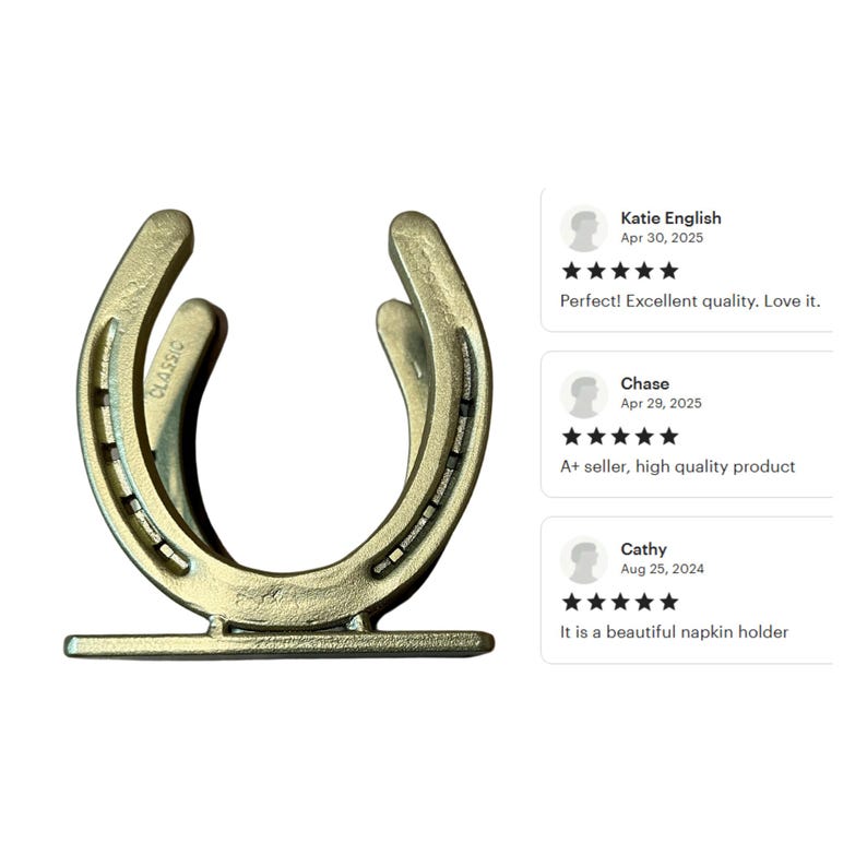 May include: A gold-toned metal napkin holder shaped like a horseshoe, featuring a flat rectangular base and the word CLASSIC embossed on the side. The design includes two parallel horseshoe-shaped frames connected to a stable bottom support piece.