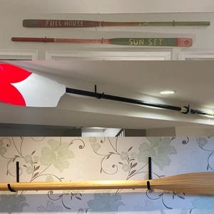 May include: Three wooden oars are hanging on the wall. The top oar is painted green and has the words "SUN SET" written on it. The middle oar is painted brown and has the words "FULL HOUSE" written on it. The bottom oar is natural wood.