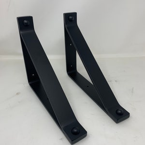May include: Two black metal shelf brackets with rounded edges and a triangular shape.