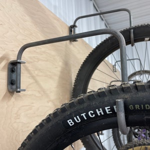 May include: Close-up of a metal bike rack mounted to a wall. The rack is holding a bicycle tire with the words "Butcher Grid Trail" printed on the side.