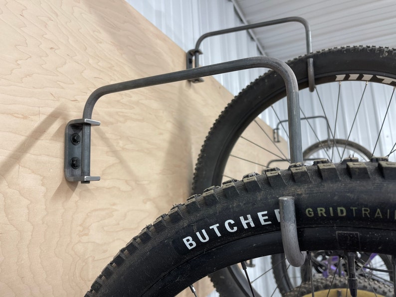 May include: Close-up of a metal bike rack mounted to a wall. The rack is holding a bicycle tire with the words "Butcher Grid Trail" printed on the side.