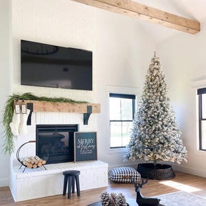 May include: A cozy living room decorated for Christmas. A large, flocked Christmas tree stands next to a fireplace with stockings. A black coffee table holds pine cones and a candle. A sign reads "Merry Christmas."