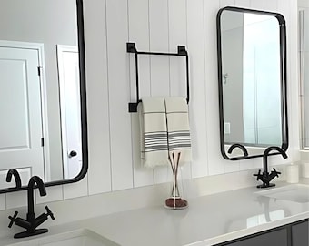 May include: A white bathroom with two black framed mirrors, a black towel rack with a white and gray striped towel hanging on it, and two black faucets with white porcelain sinks.