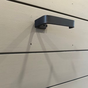 May include: A black metal towel bar mounted on a light beige wall.