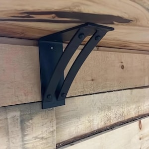 May include: Black metal shelf bracket with a curved design, mounted to a wooden wall.
