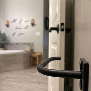 May include: Black metal towel bar mounted on a white door. The towel bar is curved and has a simple design.