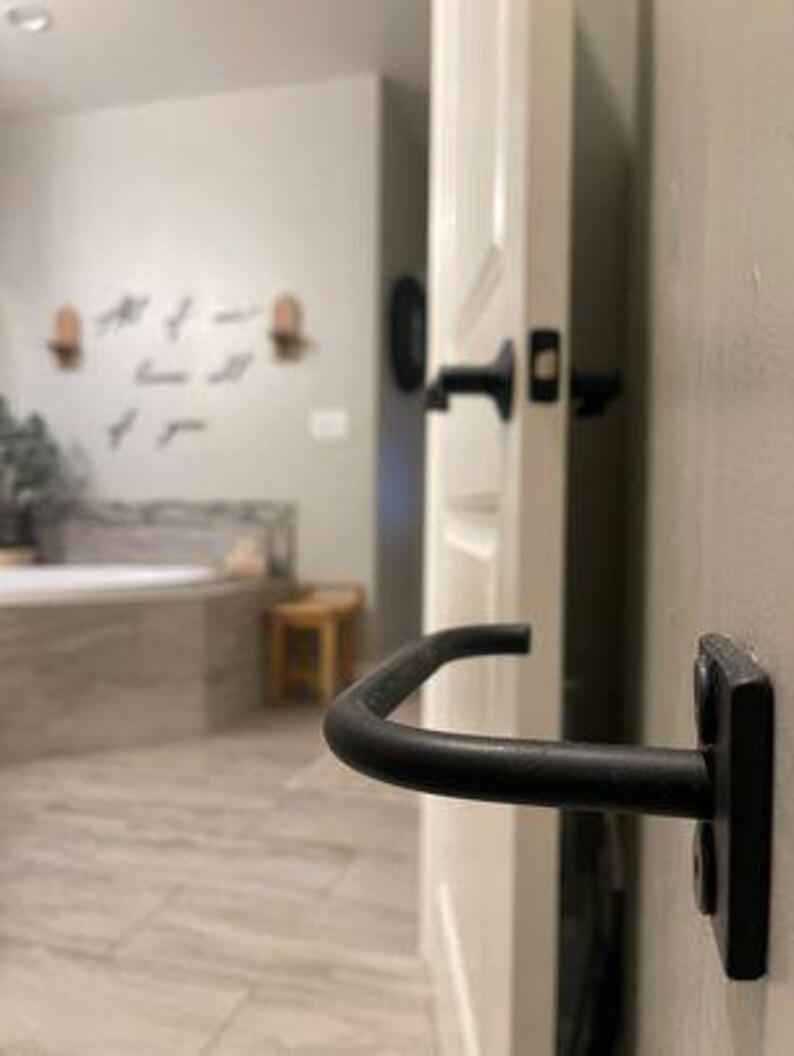 May include: Black metal towel bar mounted on a white door. The towel bar is curved and has a simple design.