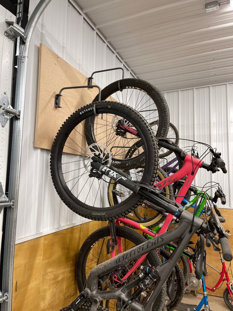 May include: A wall-mounted bike rack with multiple bikes hanging from it. The bikes are a mix of colors, including black, red, green, and blue. The rack is made of metal and has a wooden backing.