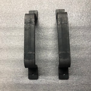 May include: Two black metal door handles with a simple, curved design. The handles are mounted on a gray background.