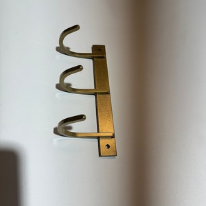 May include: Gold metal wall mounted hook rack with three hooks.
