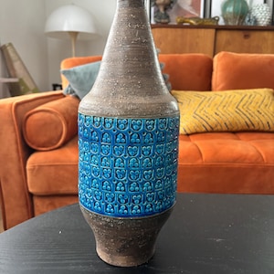 Peut inclure: Un grand vase en céramique marron avec une surface texturée et une bande de carreaux de fleurs bleues. Le vase a un col étroit et une base large. La bande de carreaux bleus présente un motif répétitif de fleurs stylisées.