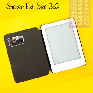 May include: An e-reader with a white border and a black cover, next to a sticker that says "New Kind Collection". The text "Sticker Est. Size 3x2" is above the e-reader. The background is yellow.