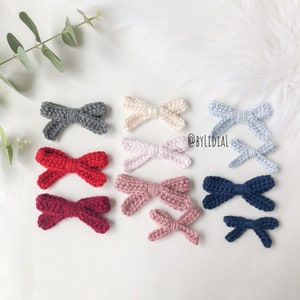 Può includere: Assortimento di fiocchi all'uncinetto fatti a mano in vari colori, tra cui grigio, rosso, rosa, crema, blu e blu navy. I fiocchi sono disposti in file su uno sfondo bianco. @BYLIDIAL è scritto nell'immagine.