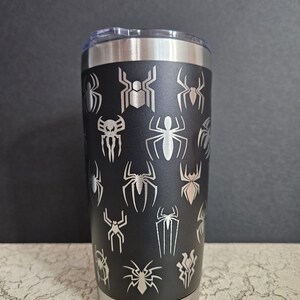 Puede incluir: Un vaso de acero inoxidable negro con varios dise&ntilde;os grabados en el lateral, con tem&aacute;tica de Spider-Man.